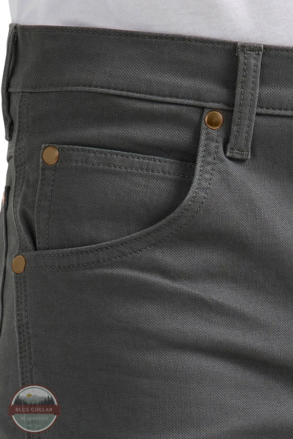 Close-up of gray pants with gold buttons and a visible brand logo. Wrangler 112361474 Premium Performance Tough Comfort Cowboy Cut Slim Fit Canvas Jean in Grey Pinstripe front pocket view
