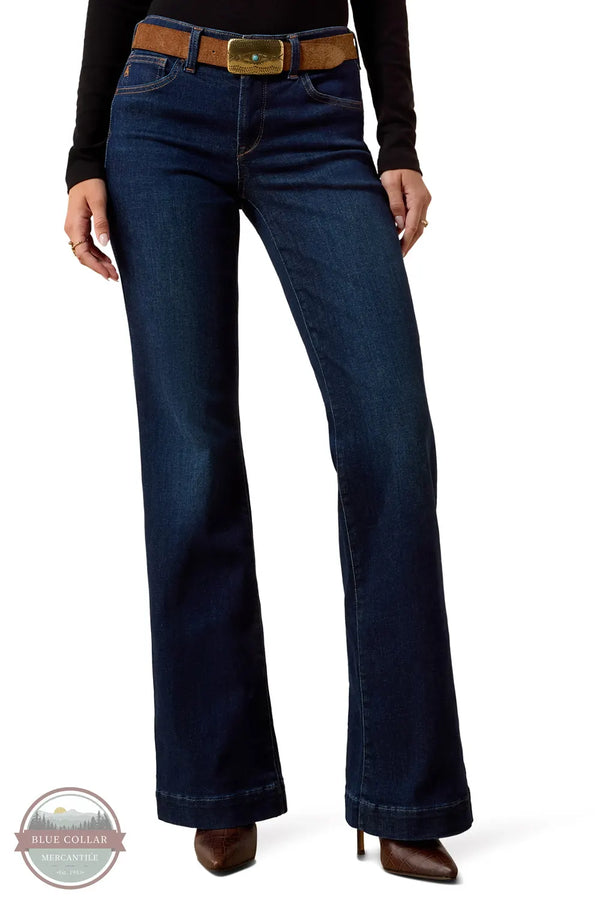Ariat 10079195 Women's Perfect Rise Vilma Ultrastretch Trouser Jeans in Hayward, A model wearing dark blue flare jeans with a brown belt, a black long-sleeve top, and brown heeled boots, shown from the waist down on a white background.