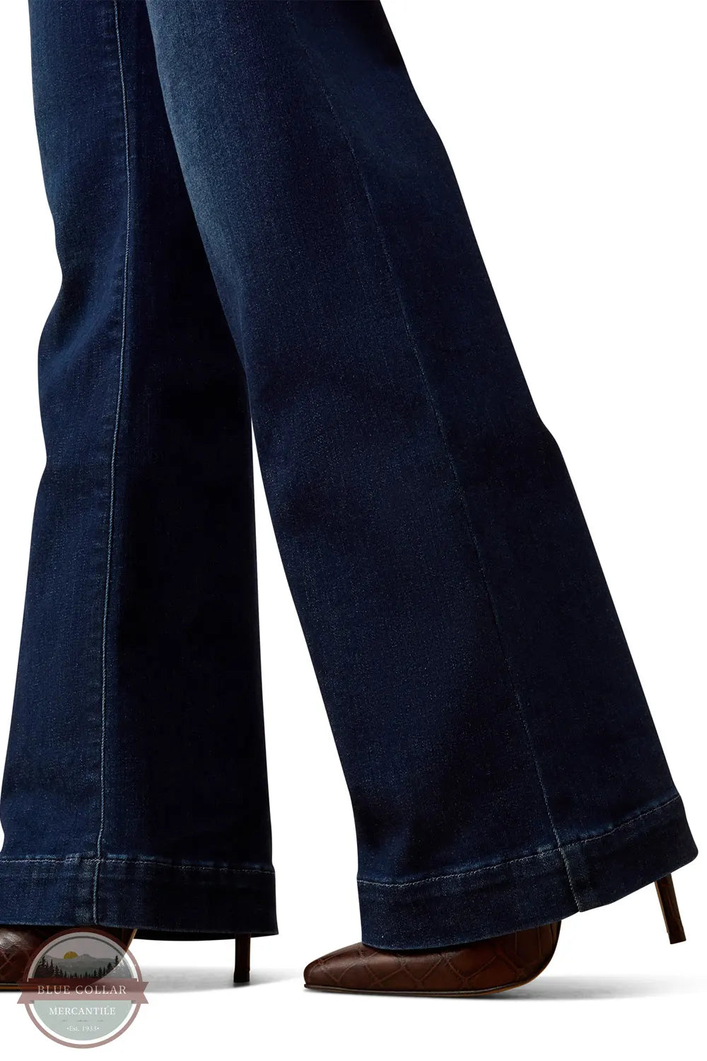 Ariat 10079195 Women's Perfect Rise Vilma Ultrastretch Trouser Jeans in Hayward, Close-up of a person's legs wearing dark blue flared jeans and brown pointed-toe heels against a white background.