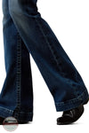 Ariat 10079240 Women's High Rise Teresa Slim Trouser Jeans in Decatur, Close-up of a person's legs wearing dark blue flared jeans and black shoes against a white background.