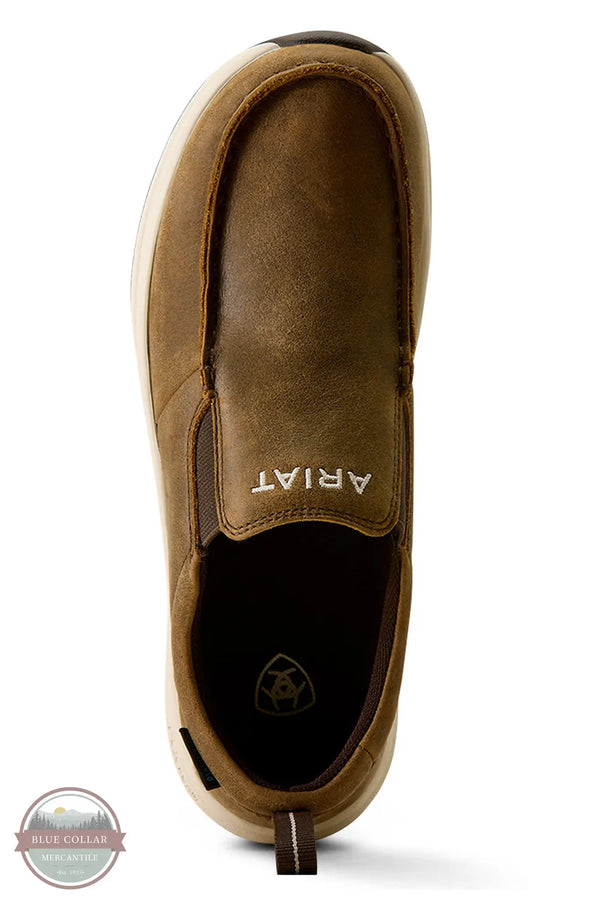 Ariat's 10080297 Women's Buckeye Slip On Waterproof Shoe in Brown Bomber, A single brown slip-on shoe shown from a top-down view on a white background, with the ARIAT brand name visible on the side and a circular 'Blue Collar' watermark in the bottom-left corner.