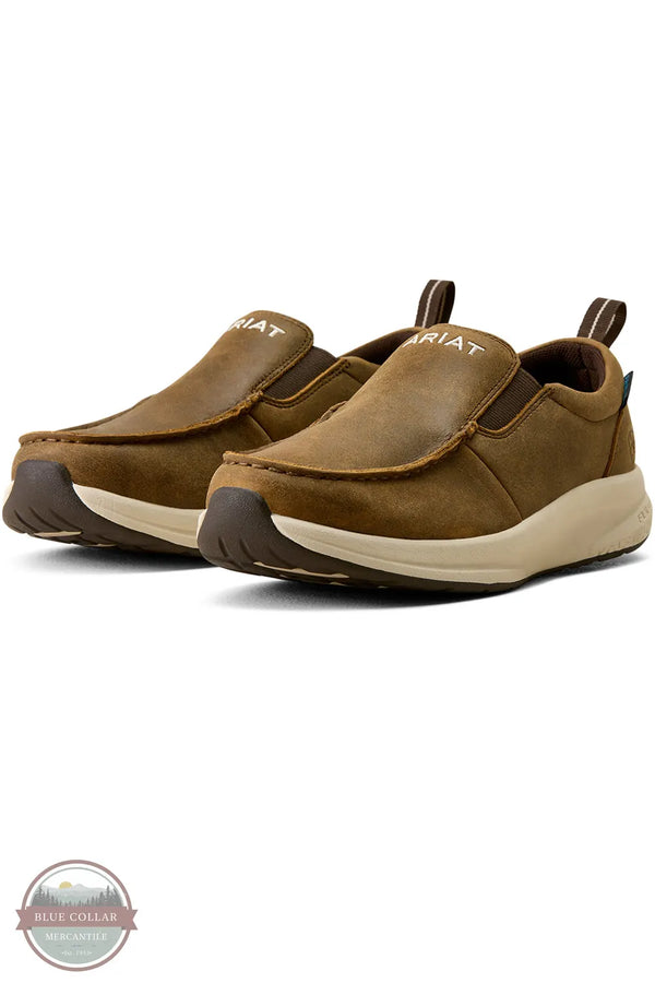 Ariat's 10080297 Women's Buckeye Slip On Waterproof Shoe in Brown Bomber, A pair of Ariat slip-on shoes in brown suede and leather, featuring a cream midsole and a dark brown outsole, shown on a white background with a Blue Coral watermark in the lower-left corner.