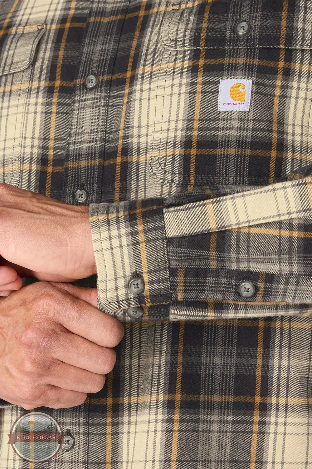 Carhartt 107013-N04 Men's Hubbard Loose Fit Long Sleeve Flannel Plaid Shirt, Close-up of a Carhartt plaid button-up shirt with a person's hands adjusting the cuff, showing the fabric texture and the brand label on the chest.