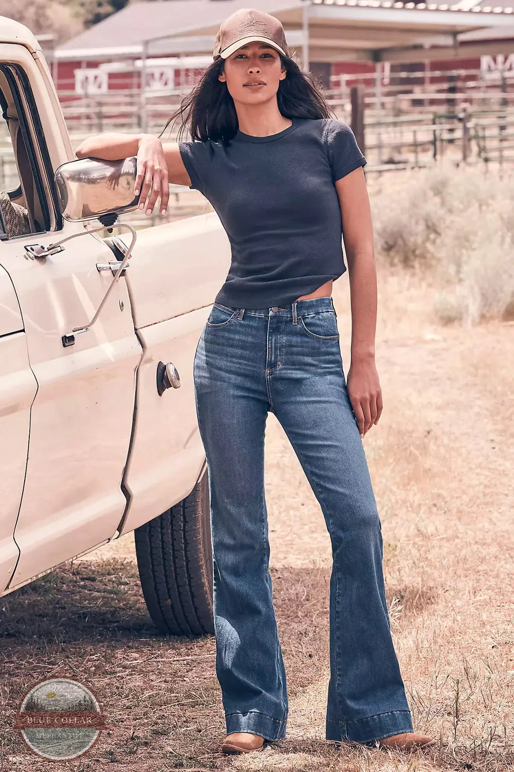 Wrangler 112382765 Women's Bespoke High Rise Trouser Jean in Reina lifestyle image of woman in jeans leaning on truck