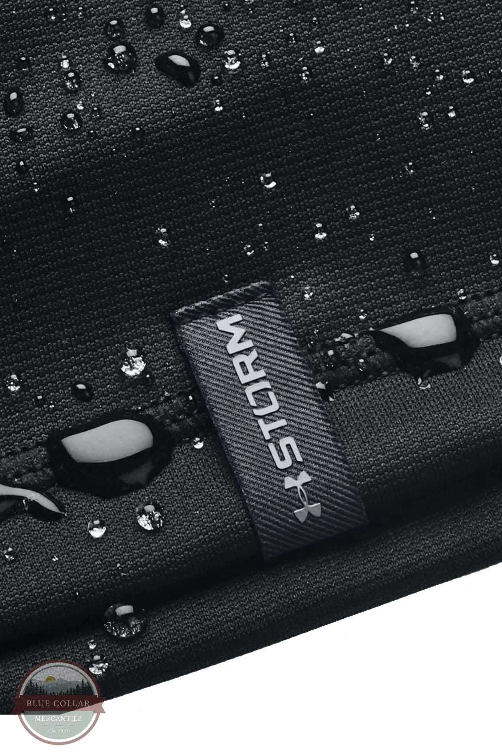 Under Armour 1365918 UA Men's Storm Beanie, Close-up of a black textured fabric item with water droplets on the surface and a dark gray woven label reading STORM.