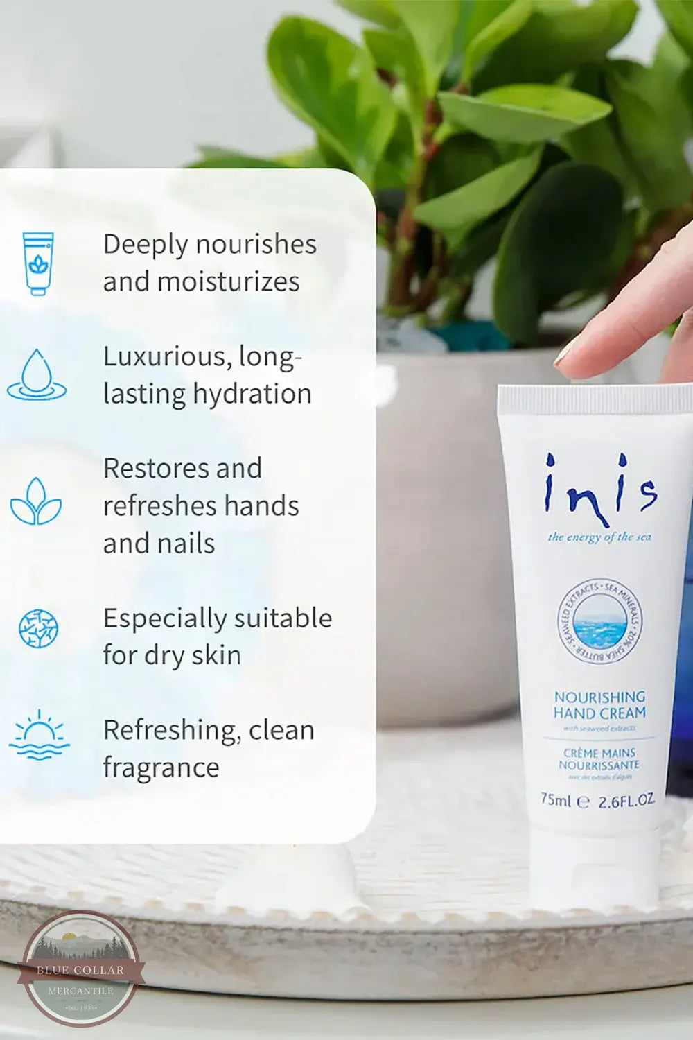Inis 8015556 Nourishing Hand Cream 2.6FL. OZ. A hand holds an Inis Nourishing Hand Cream tube next to a white informational card highlighting product benefits, with a blurred green potted plant in the background.