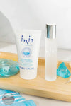 Inis 8016119 Traveler Duo Set Body Lotion and Cologne, Inis Revitalising Body Lotion in a white squeeze tube next to a frosted glass spray bottle with a silver cap, styled on a wooden tray with blue decorative stones.