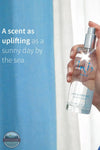 Inis 8020901 Home &amp; Linen Mist 3.3fl. oz., A hand holds a clear perfume bottle labeled 'inis' against a bright blue and white curtain background, with promotional text on the left.