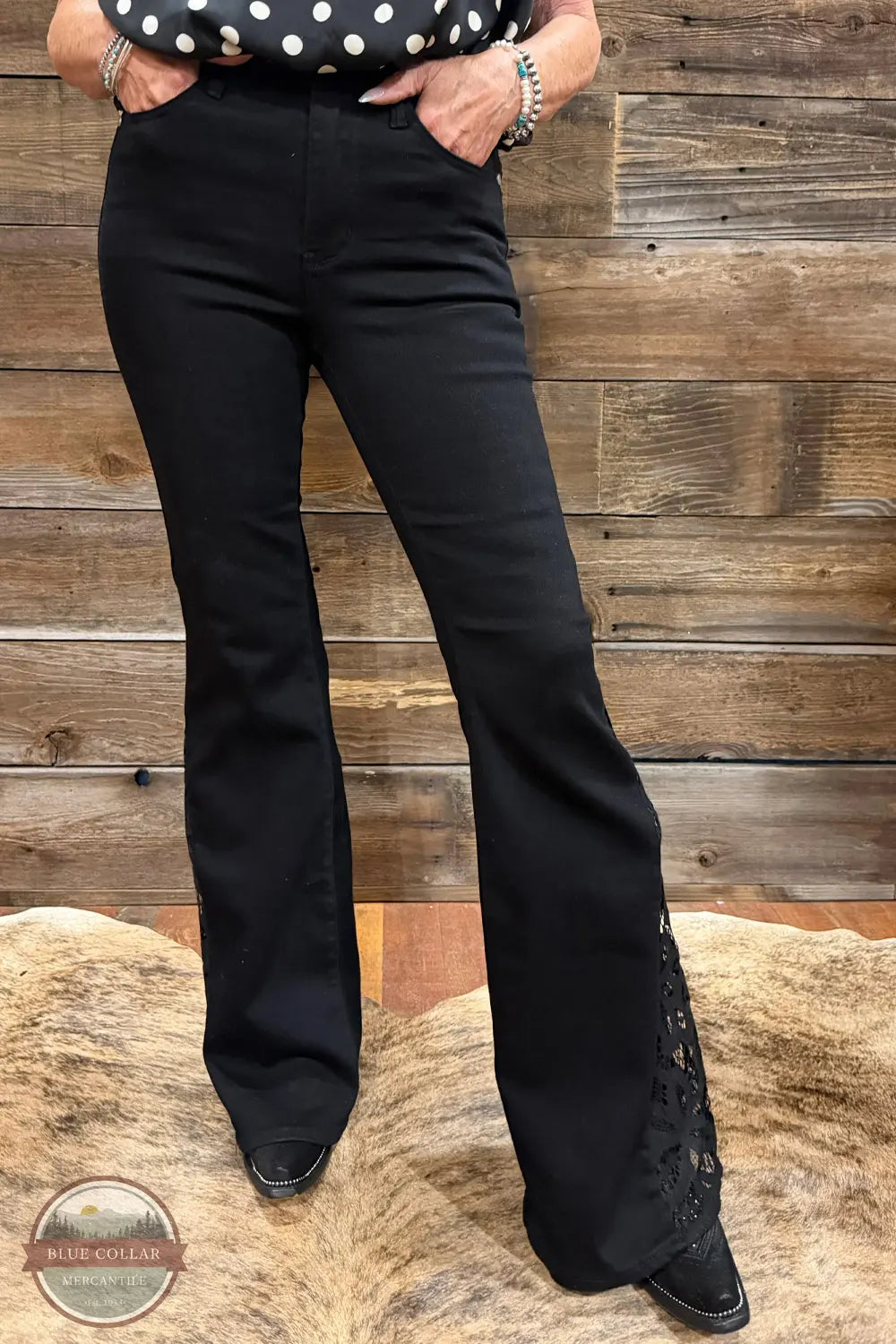 Judy Blue 881177REG High Waist Black Jaqueline Flare Jean With Lace, Black flare jeans with lace-up detailing on the outer sides, shown on a model standing on a cowhide rug against a rustic wood plank wall.