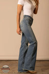 Person wearing blue flared jeans and a white top against a beige background Kimes Ranch WJE0000016 Olivia light wash side

